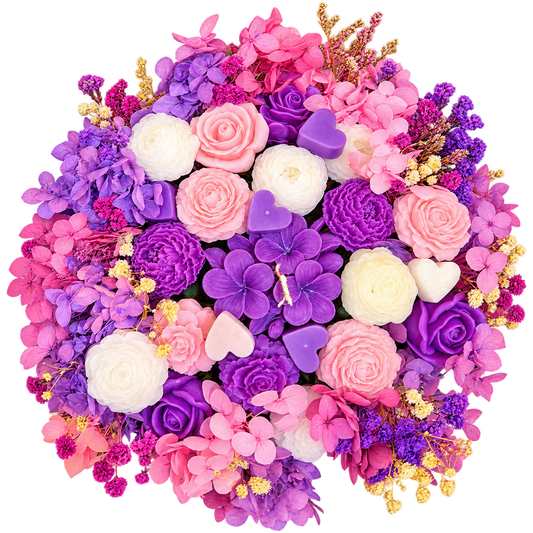 A dense, round floral bouquet featuring a mix of pink, purple, and white artificial flowers, including roses, hydrangeas, and carnations, accented with small white and purple heart-shaped candles and gold filler stems, isolated on a white background.
